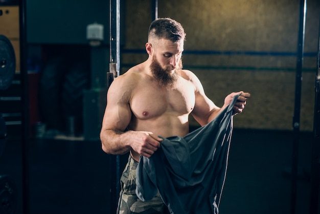 Muskularny atrakcyjny przystojny kaukaski Brodaty mężczyzna trzyma koszulkę w siłowni crossfit.