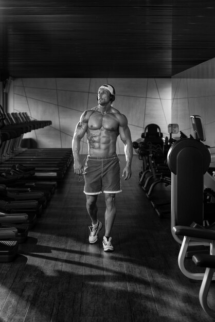 Muskularny dojrzały mężczyzna słuchający muzyki ze swojego odtwarzacza MP3 w nowoczesnym centrum fitness