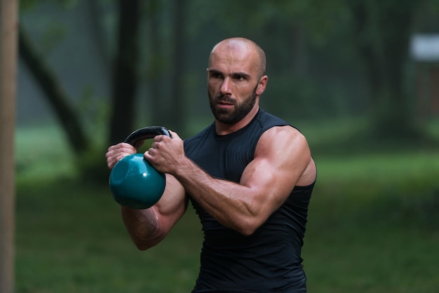 Muskularny dorosły mężczyzna rasy kaukaskiej ćwiczący na świeżym powietrzu z kettlebell