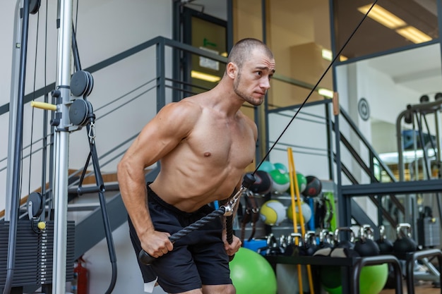 Muskularny kulturysta przystojny mężczyzna z nagim torsem trenuje triceps na maszynie do ćwiczeń ze skrzyżowanymi kablami w nowoczesnej siłowni
