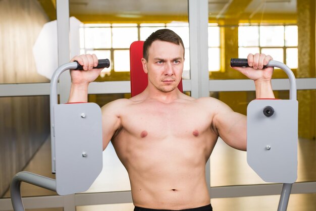 Muskularny mężczyzna bez koszuli ćwiczy w siłowni.