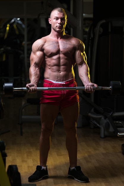Muskularny mężczyzna ćwiczący biceps ze sztangą