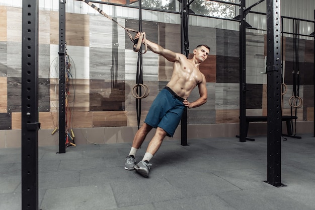 Muskularny mężczyzna ćwiczący z systemem oporu w nowoczesnym klubie. Trening funkcjonalny