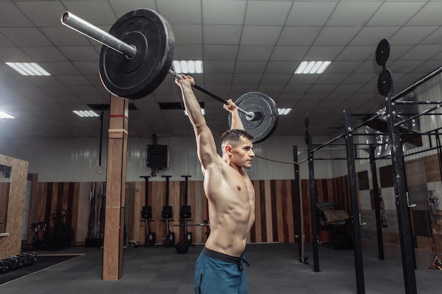 Muskularny mężczyzna ćwiczy ciężką sztangę nad głową w nowoczesnym klubie fitness. Kulturystyka i fitness