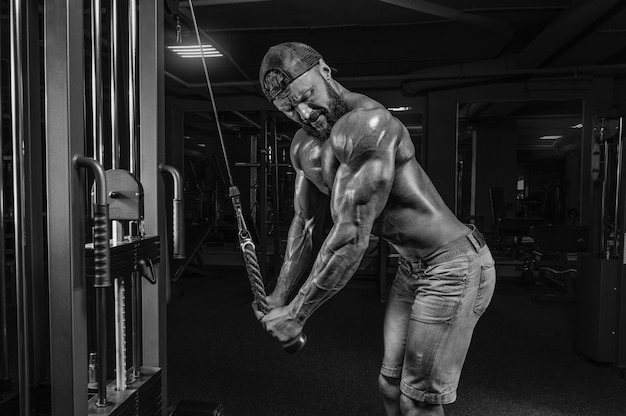 Muskularny mężczyzna ćwiczy na siłowni. Ćwiczenia na triceps. Koncepcja fitness i kulturystyki. Różne środki przekazu