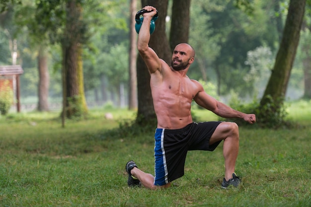 Muskularny mężczyzna fitness Balance Kettlebells z jedną ręką ćwiczenie na świeżym powietrzu