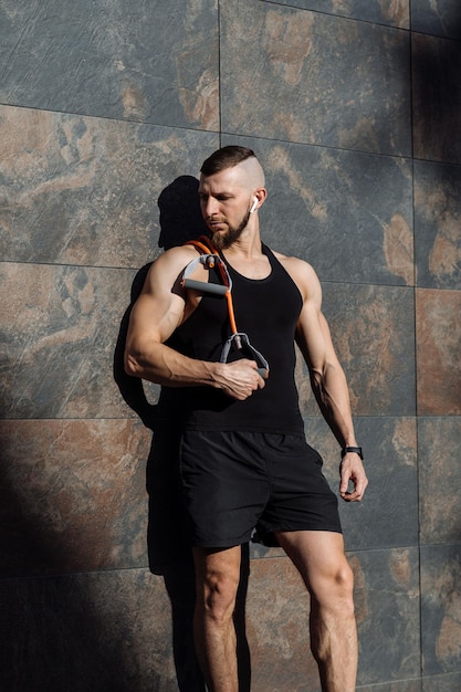 Muskularny mężczyzna lub trener fitness z rozciągającą się gumą gimnastyczną pozuje do betonowej ściany