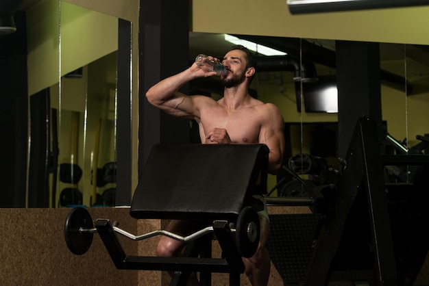 Muskularny mężczyzna odpoczywa po ćwiczeniach i piciu wody