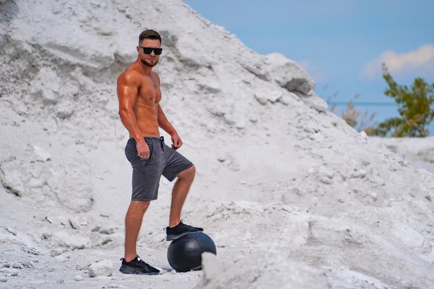 Muskularny mężczyzna pozuje na białej piaszczystej plaży z piłką fitness
