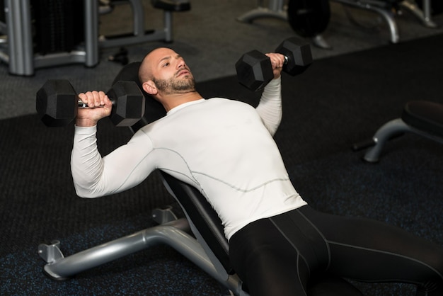 Muskularny mężczyzna robi ćwiczenia na klatkę piersiową z hantlami