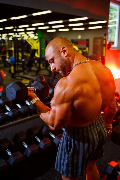 Muskularny mężczyzna shirtless robi ćwiczenia bicepsa z ćwiczeniami z hantlami jako część jego treningu kulturystycznego. Motywacja fitness, sportowy styl życia, zdrowie, wysportowana sylwetka