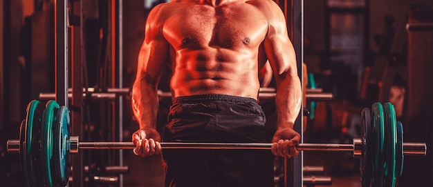 Muskularny mężczyzna trening ze sztangą na siłowni Kulturysta wysportowany mężczyzna z sześciopakem idealne ramiona abs biceps triceps klatka piersiowa