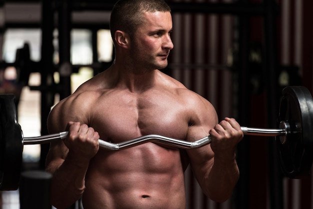 Muskularny młody mężczyzna robi duże ćwiczenia na biceps na siłowni