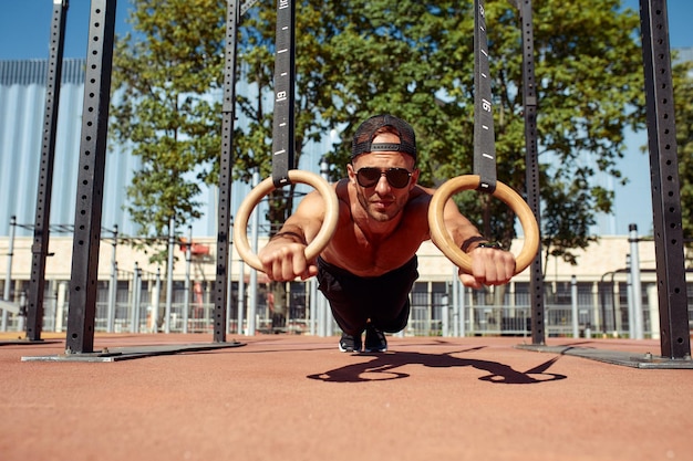 Muskularny sportowiec ćwiczący na kółkach gimnastycznych na świeżym powietrzu w siłowni na świeżym powietrzu Ręce na pierścieniach zanurzenie mężczyzna robi ćwiczenia za pomocą pierścieni