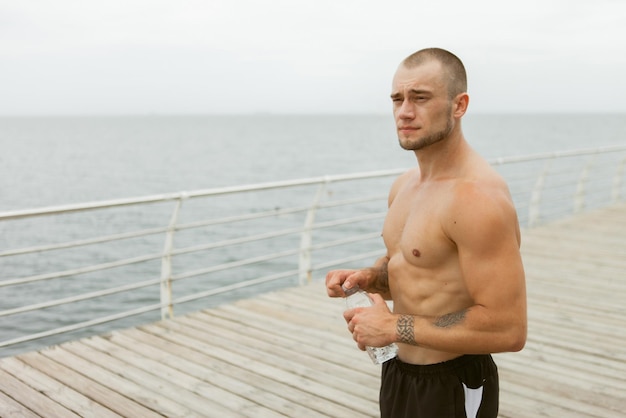 Muskularny sportowiec trzymający butelkę wody na plaży