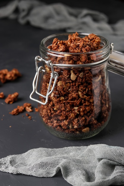 Musli chrupiące musli granola z naturalnym miodem, czekoladą i orzechami w szklanym słoju na ciemnym tle