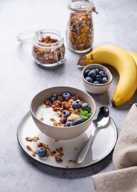 Musli z wegetariańskim jogurtem, bananem i jagodami w misce na szarym tle tekstury Zdrowa i dietetyczna domowa granola na śniadanie