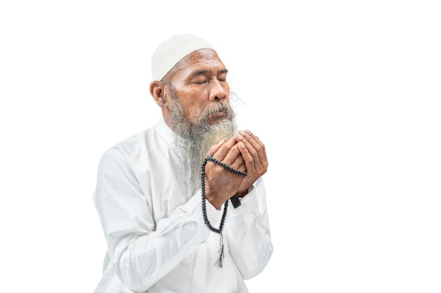 Muzułmanin z brodą w białej czapce modlący się z różańcami na rękach