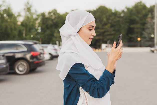 Muzułmanka młoda kobieta nosząca hidżab na głowie w mieście, wysyłając SMS-y na telefon komórkowy