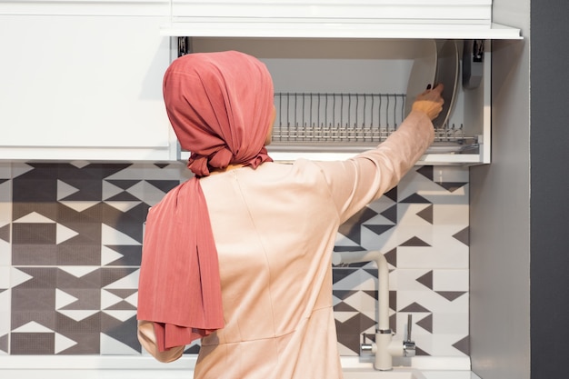 Muzułmanka w hidżabie otwiera szafki kuchenne w nowoczesnej kuchni