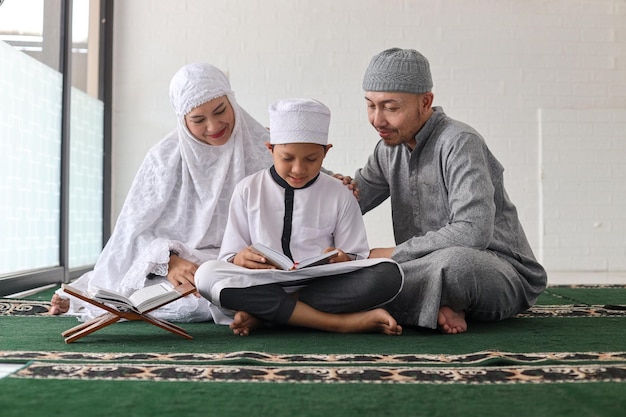 muzułmańscy rodzice z dziećmi czytającymi Koran i modlącymi się razem podczas święta ramadanu w