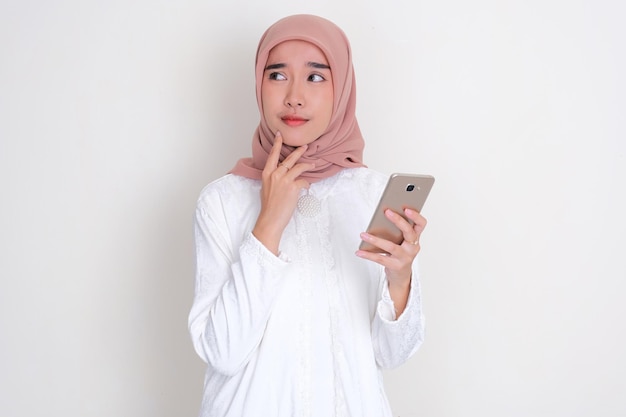 Zdjęcie muzułmańska azjatka myśli o czymś, trzymając telefon komórkowy