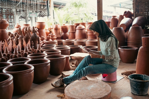 Muzułmańska dziewczyna w hidżabie siedzi za pomocą podkładki między ceramiką w sklepie z ceramiką