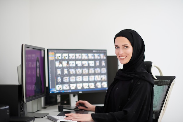 Muzułmańska graficzka pracująca na komputerze przy użyciu tabletu graficznego i dwóch monitorów. Dziewczyna w hidżabie edytuje zdjęcia w biurze