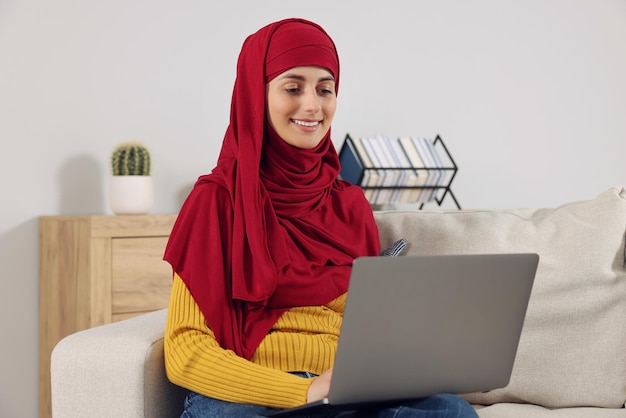 Muzułmańska kobieta używająca laptopa na kanapie w pokoju