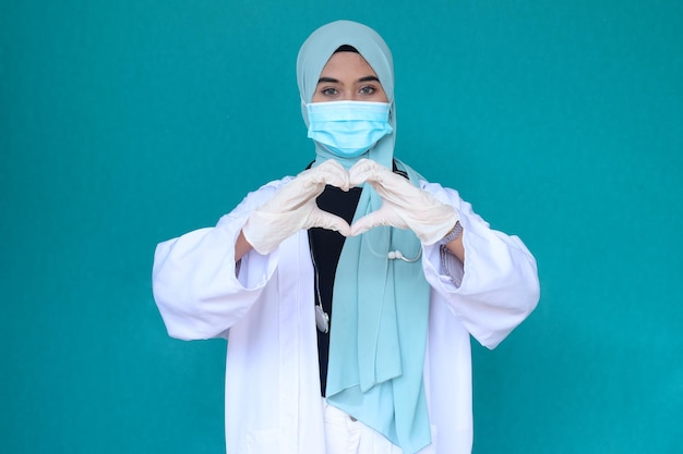 Muzułmańska lekarka z maską ochronną i rękawiczkami gestykuluje symbol serca na klatce piersiowej