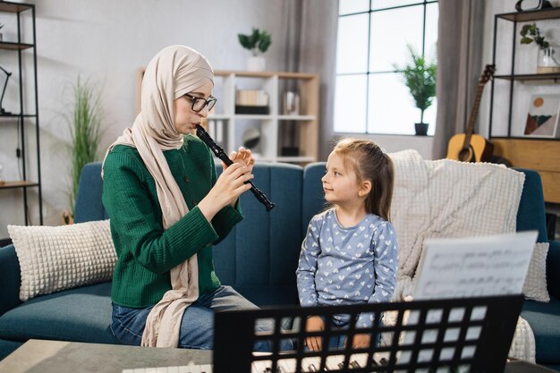 Muzułmańska mama i mała szczęśliwa dziewczynka w muzykoterapii, grając na flecie w pokoju muzycznym