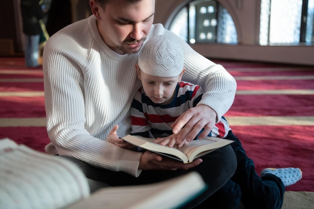 muzułmańska modlitwa ojciec i syn w meczecie modlą się i czytają razem świętą księgę koranu koncepcja edukacji islamskiej