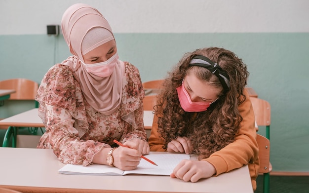 Muzułmańska nauczycielka hidżabu pomaga dzieciom w szkole ukończyć lekcję w klasie.