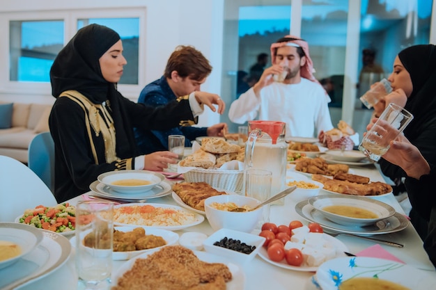 Muzułmańska rodzina spożywająca obiad z iftar, pijąca wodę, aby przerwać ucztę. Jedzenie tradycyjnych potraw podczas miesiąca biesiadowania Ramadanu w domu. Islamskie jedzenie i picie halal w nowoczesnym domu.