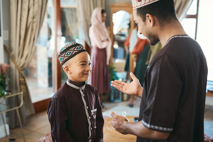 Zdjęcie muzułmański ojciec i syn rozmawiają i nawiązują więzi w salonie podczas święta religijnego w domu śliczny uśmiechnięty i szczęśliwy islamski chłopiec słuchający rad od swojego taty w tradycyjnym stroju