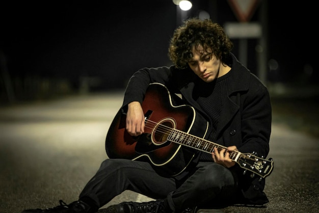 Muzyk z gitarą akustyczną sam na chodniku w nocy