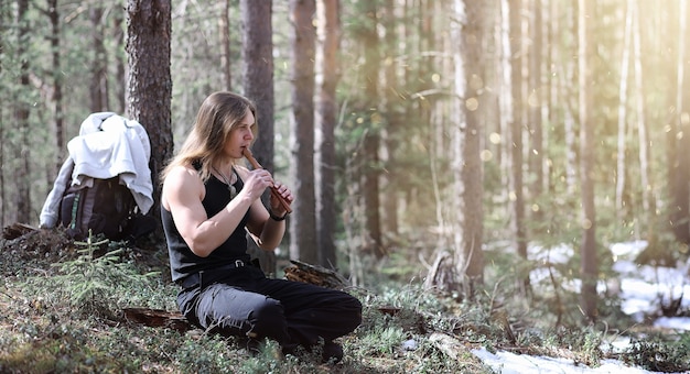 Muzyk z narzędziem w naturze. Mężczyzna gra na flecie w sosnowym lesie. Muzyka druidów w wiosennym lesie.