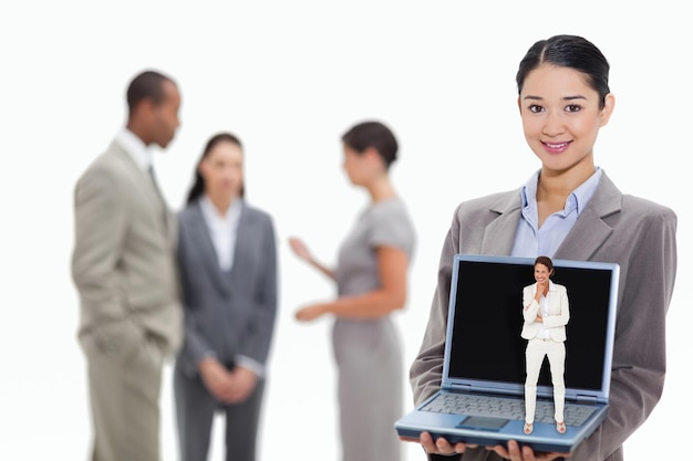 Myśląca businesswoman przeciwko businesswoman uśmiecha się, pokazując ekran laptopa ze współpracownikami w tle
