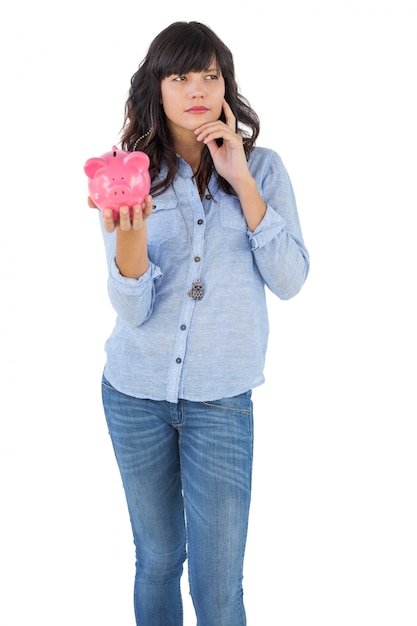 Myśląca młoda kobieta trzyma jej prosiątko banka