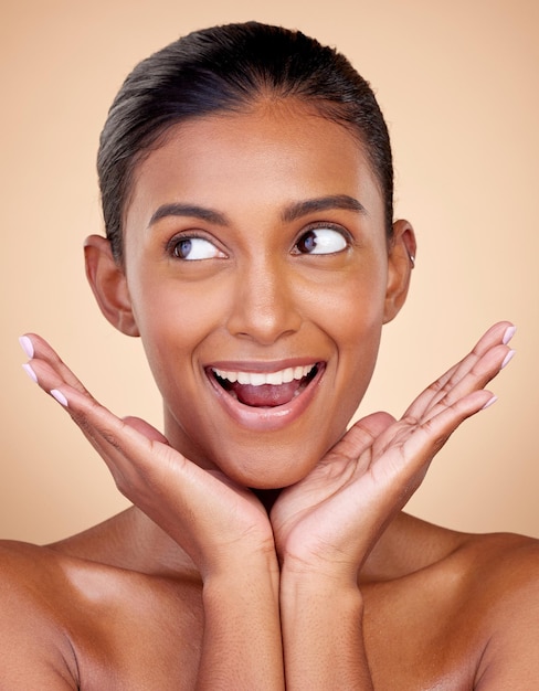 Myśląca piękność lub szczęśliwa kobieta o naturalnym blasku twarzy z dermatologicznymi kosmetykami do pielęgnacji skóry w studio Ręce w tle lub twarz indyjskiej modelki uśmiechniętej z pomysłami zdrowotnymi wellness lub miłością do siebie