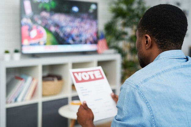 Myślący mężczyzna oglądający telewizję i trzymający dokument głosowania