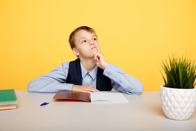 Myślący uczeń ładny chłopiec w prosess studiowania na białym tle.