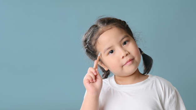 Zdjęcie myślenie mała dziewczynka dziecko azjatyckie na niebieskim tle. myślenie dziecka. burza mózgów i koncepcja pomysłu. koncepcja edukacji.