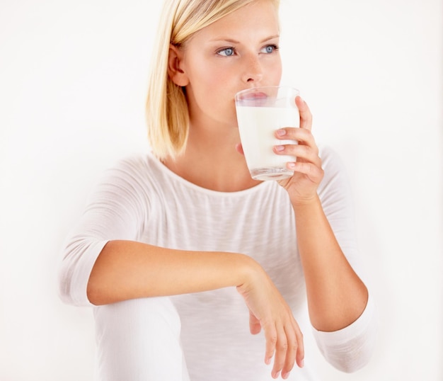 Zdjęcie myślenie o mleku i wapniu z kobietą pijącą ze szklanki w studio na białym tle odżywianie i detoksykacja ze zdrową młodą kobietą, która lubi pić witaminy lub minerały