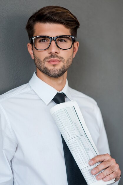 Zdjęcie myślenie o nowych rozwiązaniach. pewny siebie młody człowiek w koszuli i krawacie, trzymając gazetę