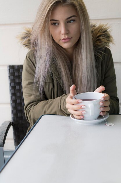 Zdjęcie myślliwa młoda kobieta pijąca kawę przy stole.