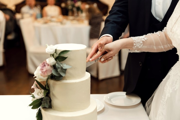 Na bankiecie weselnym panna młoda i pan młody kroją swój rustykalny tort weselny. ręce z bliska wycinające piękne ciasto