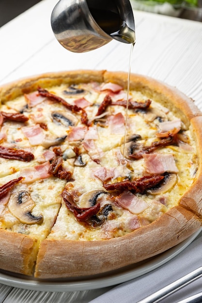 Na biały talerz wylewa się pizzę z pieczarkami i szynką.