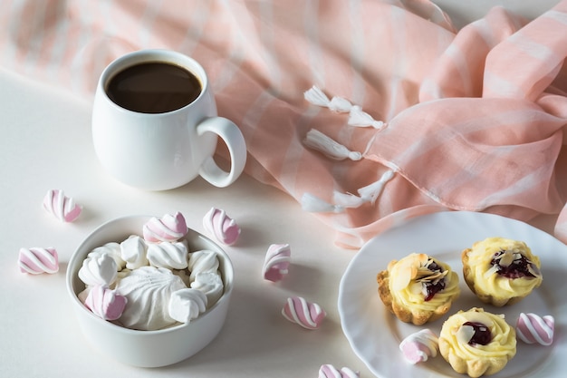 Na białym stole z różowym szalem filiżanka kawy i słodyczy