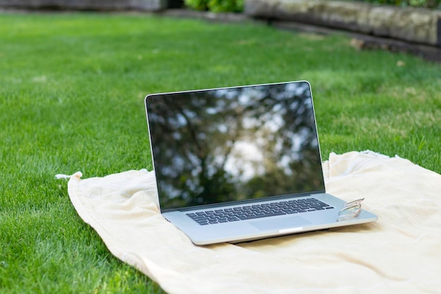 Na białym tle laptop na ręczniku w ogrodzie, w którym odbijają się liście drzew na ekranie z założonymi okularami